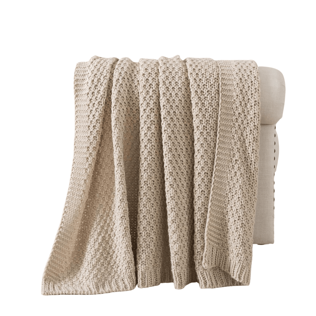 A cozy beige knitted blanket draped over the arm of a light-colored sofa.
